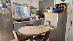 A modern kitchen with a round wooden table and two brown chairs, a stainless steel refrigerator, a sink, and various kitchen appliances. - Nice house with garden near the beach (Dives-sur-Mer)