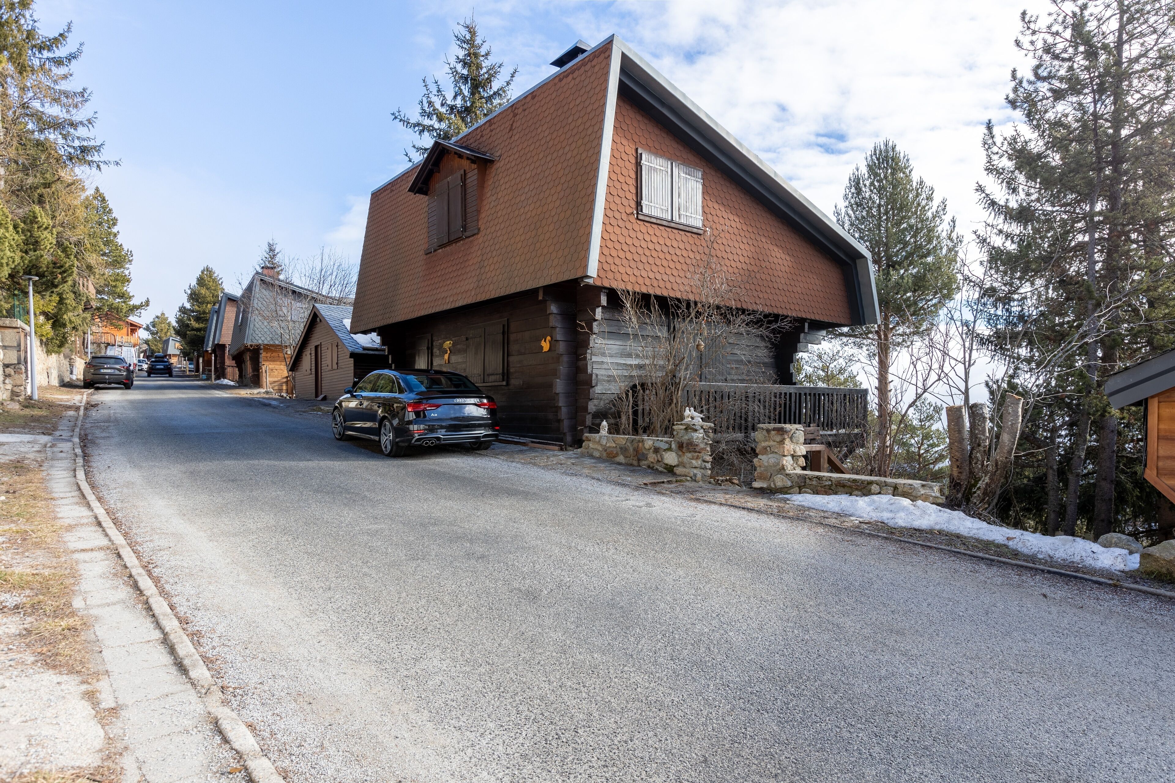 A residential street with houses, a parked car, and snow on the ground.