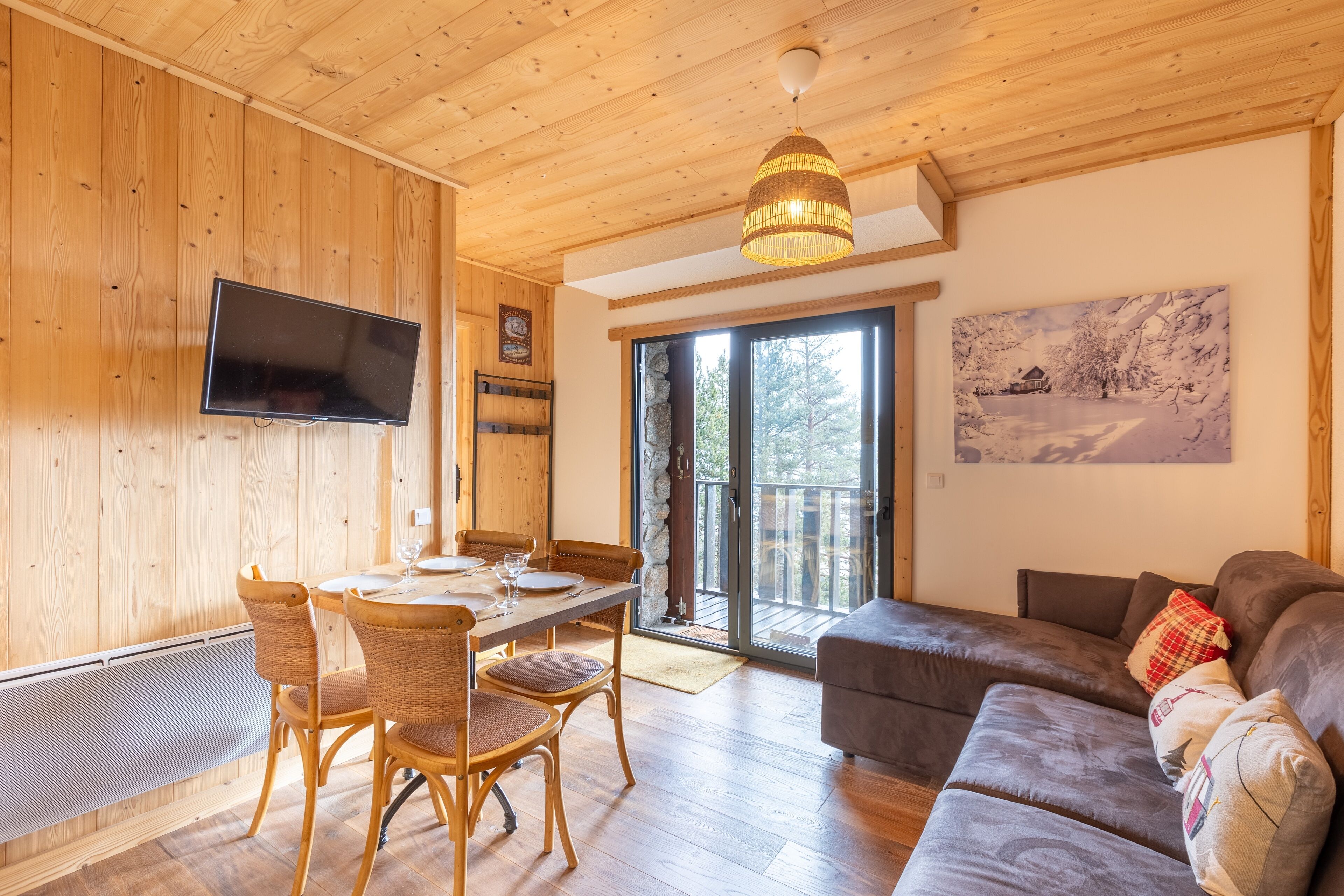 A wooden interior with a dining area, a sofa, and a TV mounted on the wall.