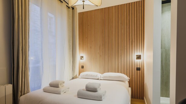 Een hotelkamer met een bed, twee kussens, een nachtkastje, een lamp en een houten wandpaneel.