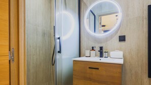 Een moderne badkamer met een douchecabine van glas, een houten wastafelmeubel met een spiegel en een witte wasbak.