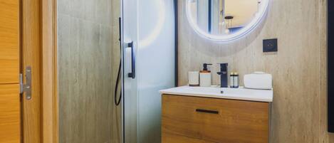 A modern bathroom with a glass shower enclosure, a wooden vanity with a mirror, and a white sink.