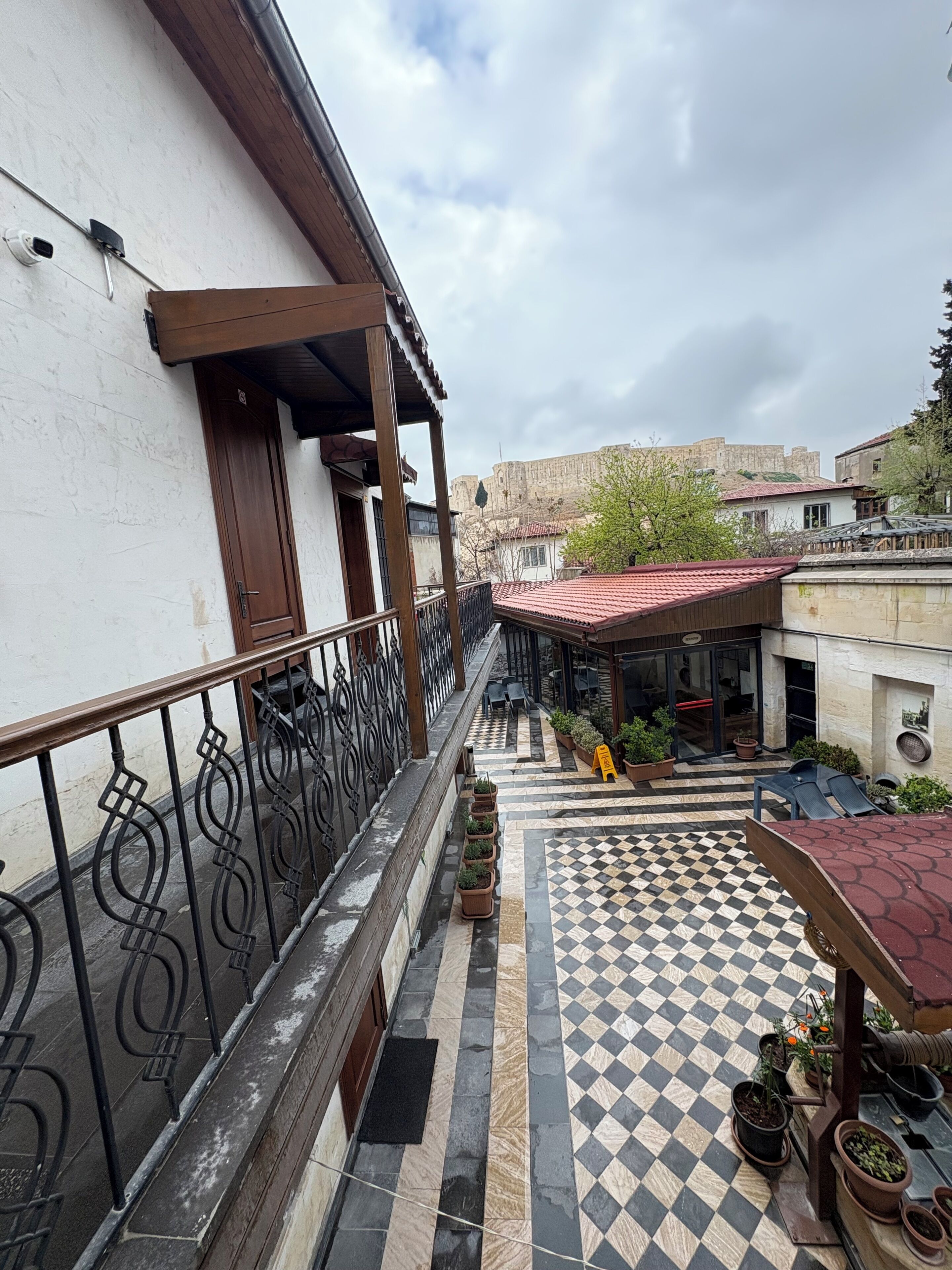 A courtyard with a checkered floor, potted plants, and a view of a historic building in the background.