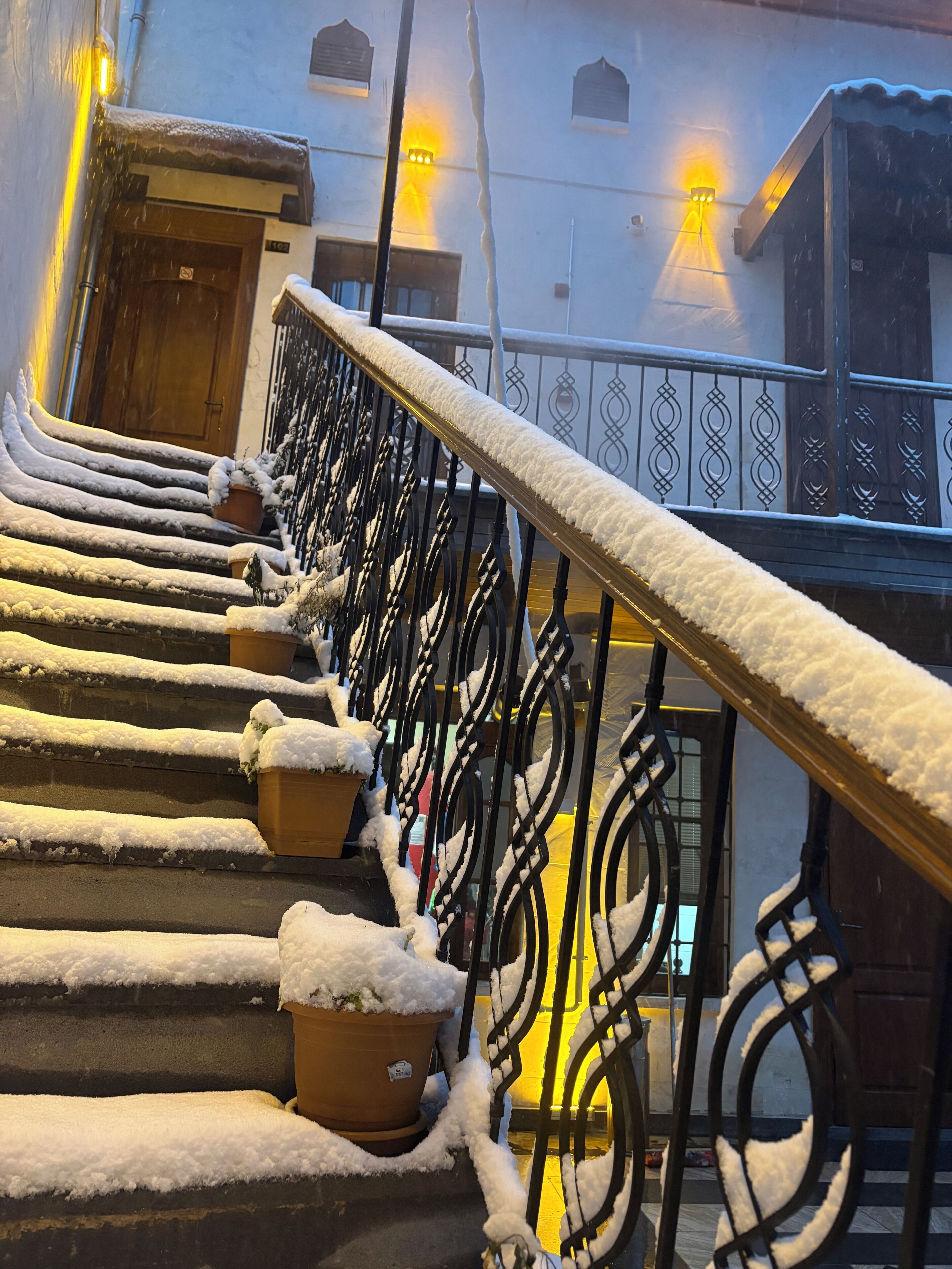Uma escadaria com degraus e corrimãos cobertos de neve, levando a uma entrada de edifício.