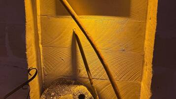 Una habitación con decoración rústica, que presenta un rastrillo de madera apoyado en la pared y una piedra giratoria.