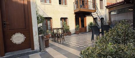 Un patio con suelo a cuadros, plantas en macetas y una puerta de madera con un letrero.