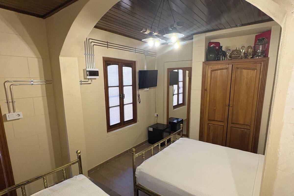 Une chambre avec deux lits, une armoire en bois, une télévision et une salle de bain avec douche.