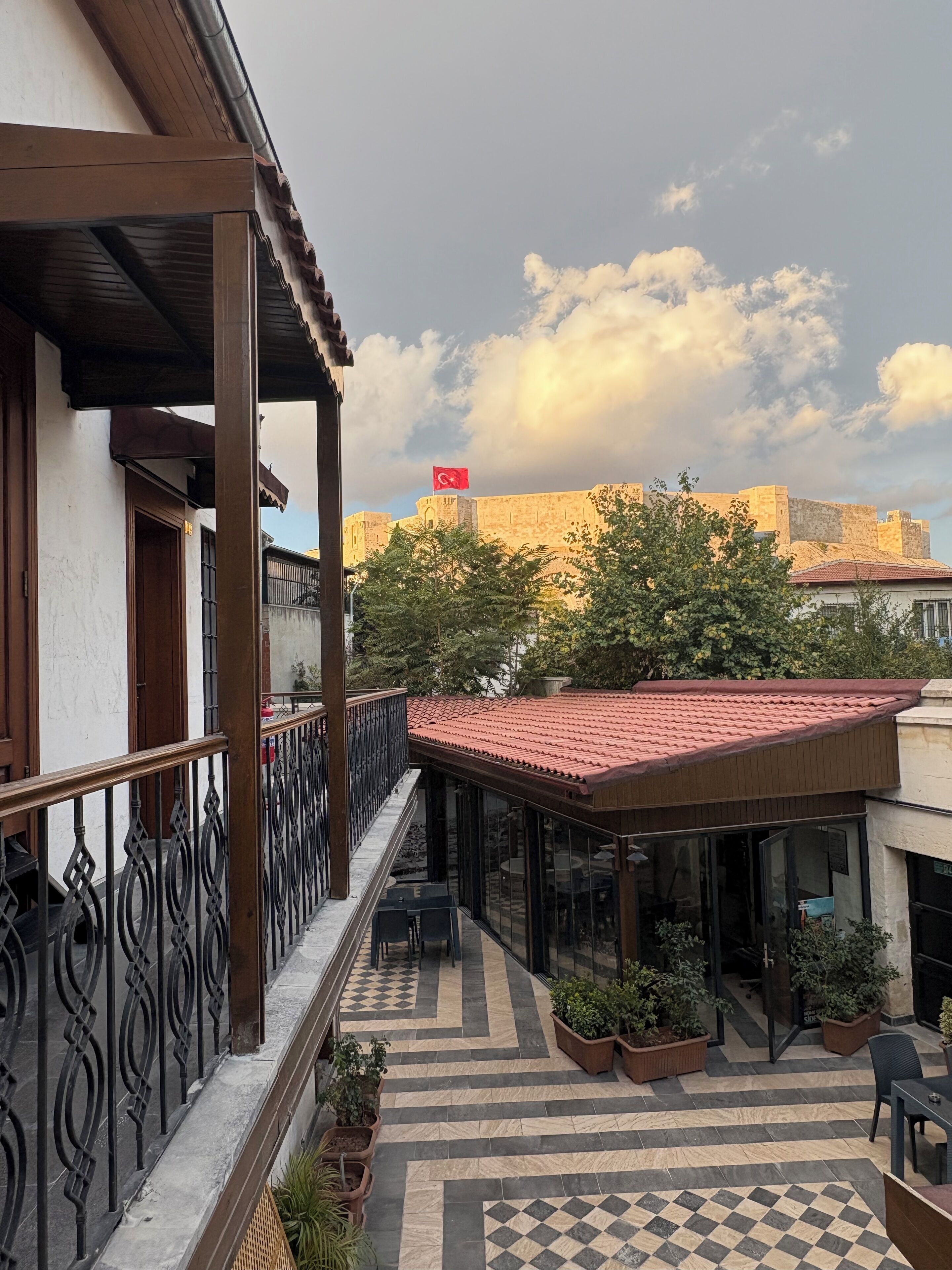 A courtyard with a checkered floor, outdoor seating, and a view of a historic building with a flag.