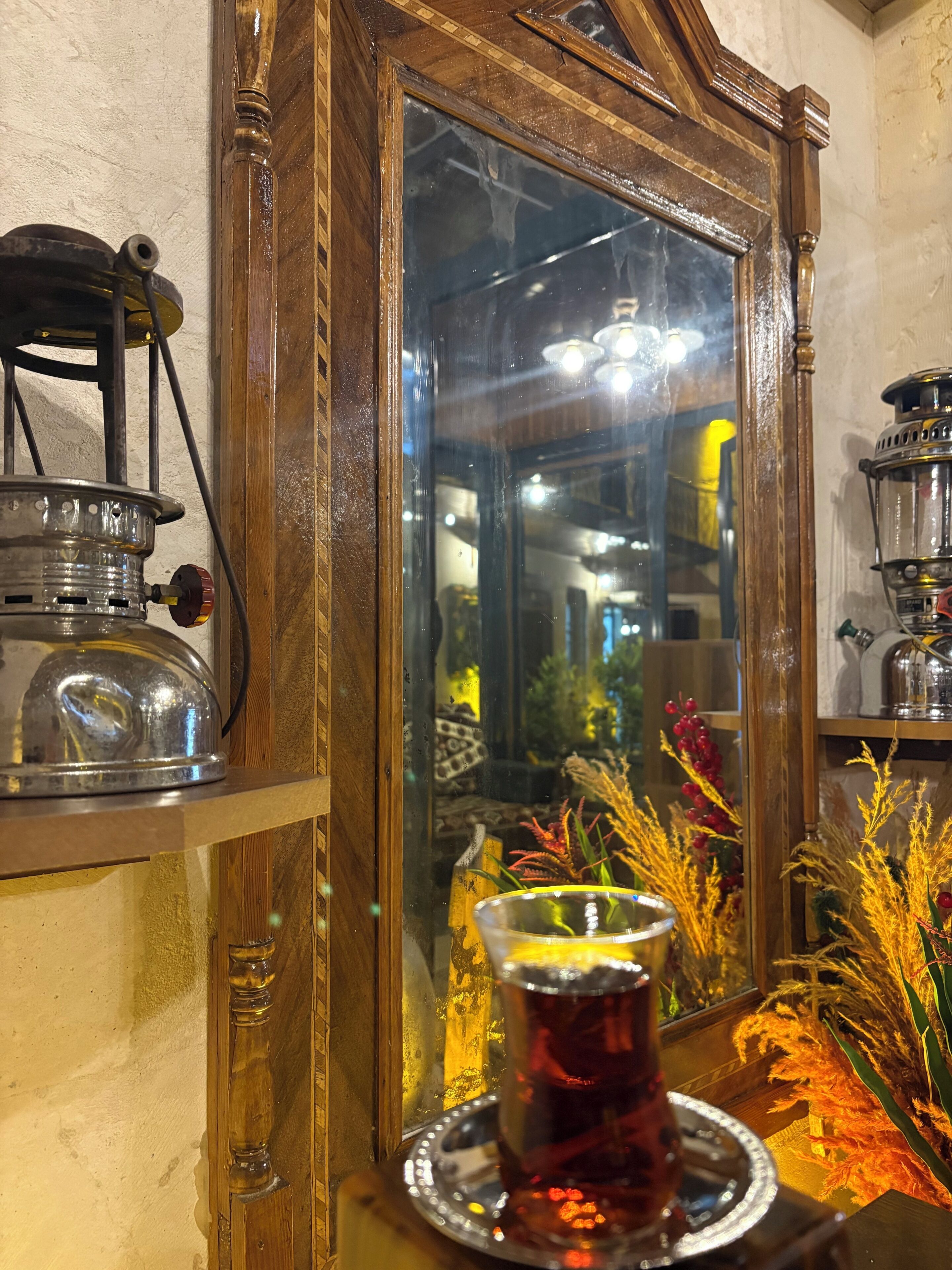 A wooden-framed mirror with a glass door, a brass lantern, and a glass pitcher on a table.