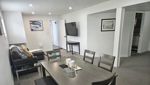 Un salon moderne avec une table à manger en bois foncé, un canapé recouvert d’un tissu gris et un téléviseur à écran plat fixé au mur.