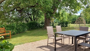Un espace extérieur aménagé avec une table et des chaises, entouré d’une végétation luxuriante et d’arbres.