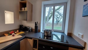 Une cuisine moderne dotée d’une grande fenêtre, d’une cuisinière encastrée et d’un plan de travail sur lequel se trouvent une planche à découper et des légumes.