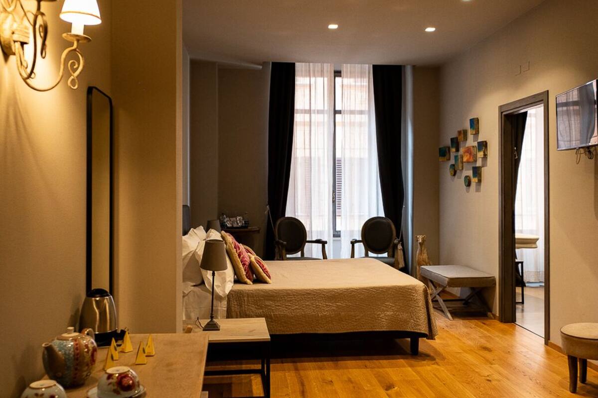 A hotel room with a wooden floor, a bed with a beige bedspread, two chairs, a small table, and a TV on the wall.