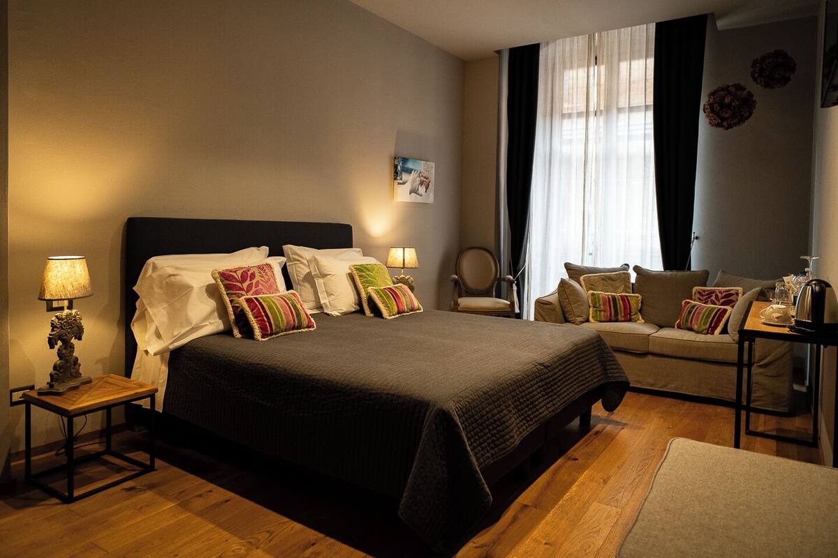 A hotel room with a large bed, a sofa, a small table, and a chair.