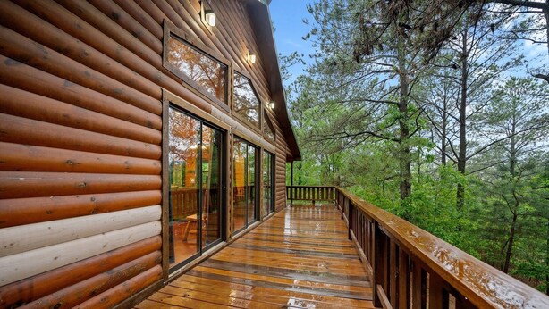 Una cabaña de madera con terraza de madera y puertas de cristal, rodeada de árboles.