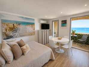 Une chambre à coucher comprenant un lit, une télévision, une table à manger avec des chaises et un balcon avec vue sur la mer.