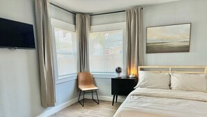 Ein Schlafzimmer mit einem Bett, einem Schreibtisch mit Lampe, einem Sessel und einem Fernseher an der Wand.