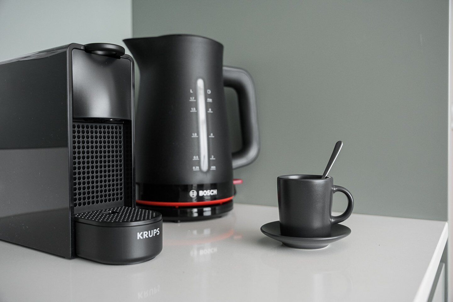 A coffee maker, a kettle, and a cup on a white countertop.