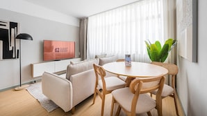 A modern living room with a sofa, a round dining table, and chairs. A television is mounted on the wall, and there is a potted plant on the table. - GuestReady - Exquisite stay in Matosinhos (Matosinhos)
