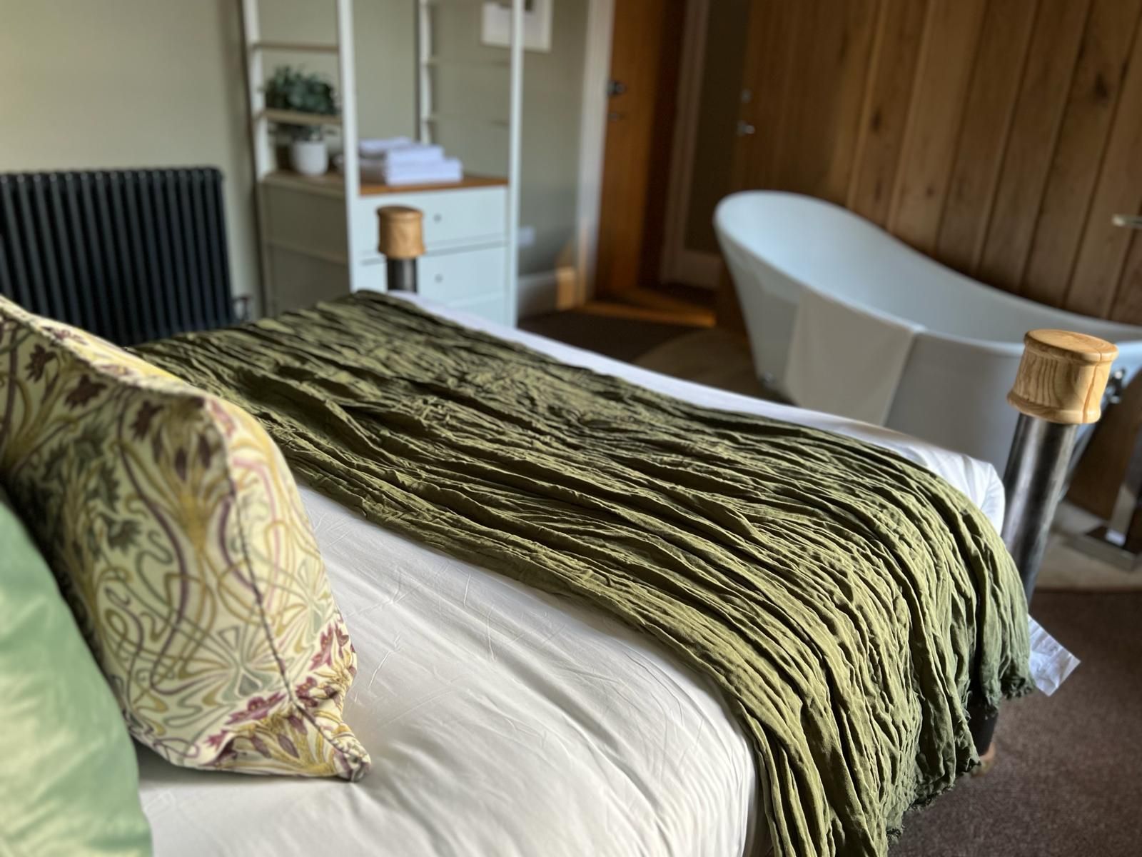 Een bed met een gekleurd kussen, een groene deken en een witte matras.