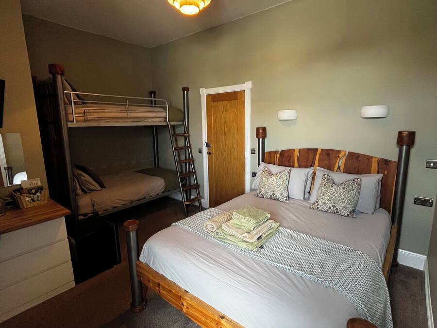 Un dormitorio con literas, una cama individual con ropa de cama estampada, un cabecero de madera, lámparas de noche y un pequeño aparador de madera.