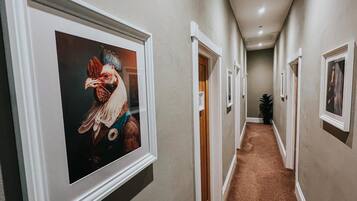A hallway with framed artwork on the walls, carpeted flooring, and doors leading to other rooms.
