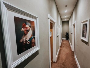 A hallway with framed artwork on the walls, carpeted flooring, and doors leading to other rooms. - The Roost (Cullompton)