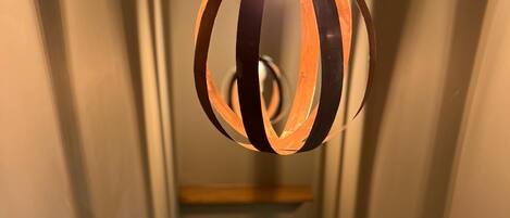 Una escalera con barandilla de madera y pasamanos metálico, que lleva a un dormitorio con cama y mesita de noche.