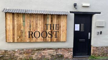 A building with a wooden sign reading 'THE ROOST' and a black door with a keypad lock.