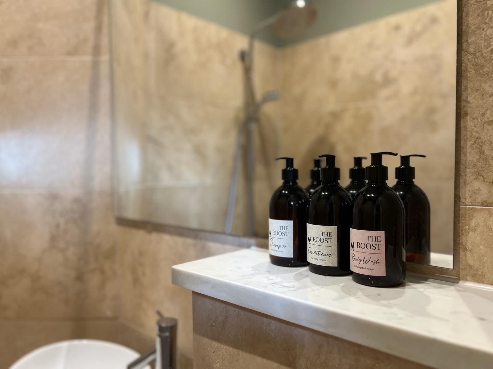 Ein Badezimmer mit Marmorwand, einer Dusche und einer Ablage mit vier Flaschen The Roost Duschgel.
