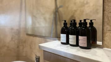 Ein Badezimmer mit Marmorwand, einer Dusche und einer Ablage mit vier Flaschen The Roost Duschgel.