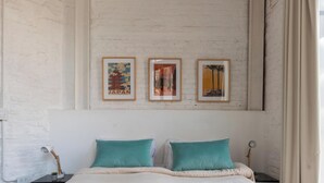 Une chambre d’hôtel avec un lit, deux oreillers, une table de chevet, une lampe et trois tableaux encadrés accrochés au mur.