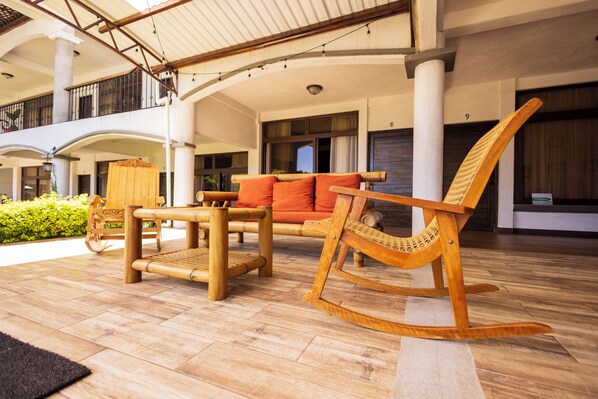 A spacious outdoor area with a wooden rocking chair, a sofa with orange cushions, and a wooden table. - Hotel Mercy (San Juan La Laguna)