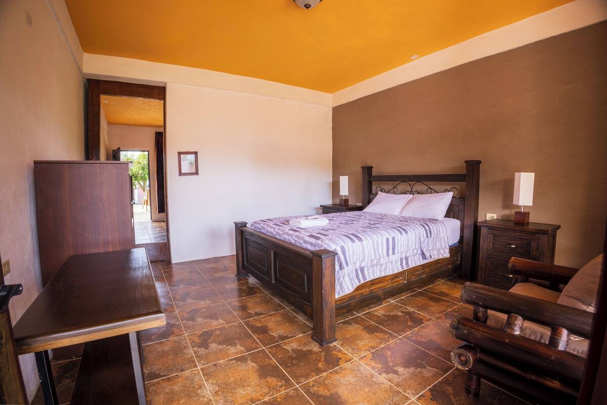 Een slaapkamer met een houten bed, bureau, stoel en nachtkastje met lamp.