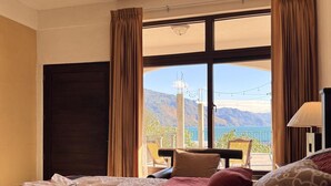 A hotel room with a large bed, a view of mountains, and a balcony with a chair.