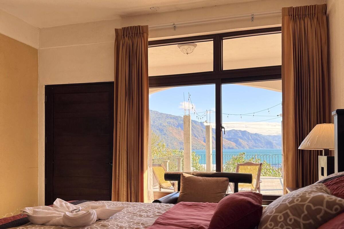Een hotelkamer met een groot bed, uitzicht op bergen en een balkon met een stoel.