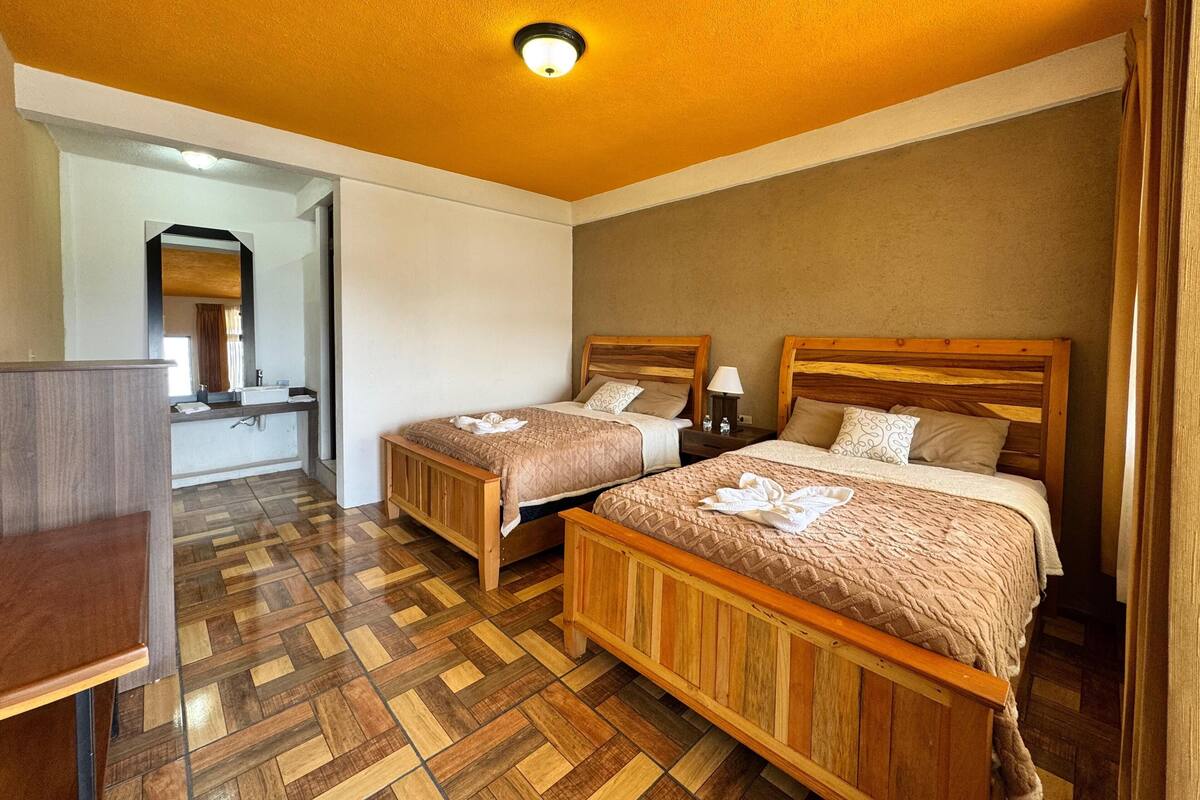 Een hotelkamer met twee houten bedden, een houten bureau, een spiegel en een badkamer met een wastafel.