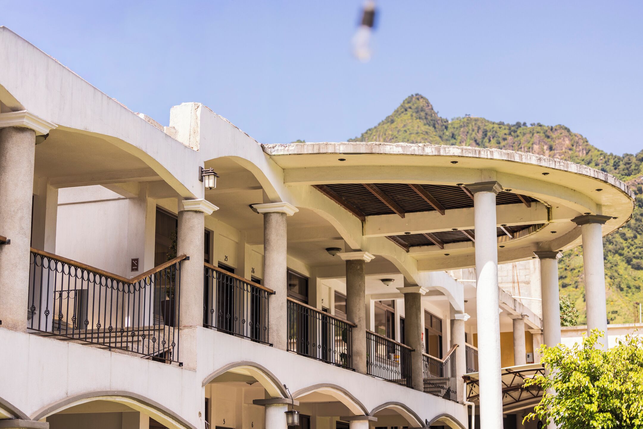 A building with multiple balconies, columns, and a mountainous backdrop.