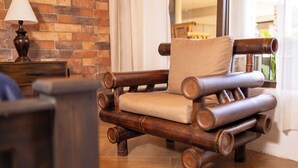 A rustic wooden chair with a cushion, a wooden side table with a lamp, and a brick wall.