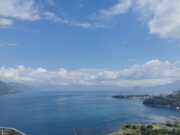 A coastal landscape with a clear view of the sea, distant mountains, and a small settlement on a nearby island. - Hotel Mercy (San Juan La Laguna)