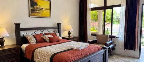A neatly arranged bedroom with a bed, bedside tables, a chair, and a large window with curtains.