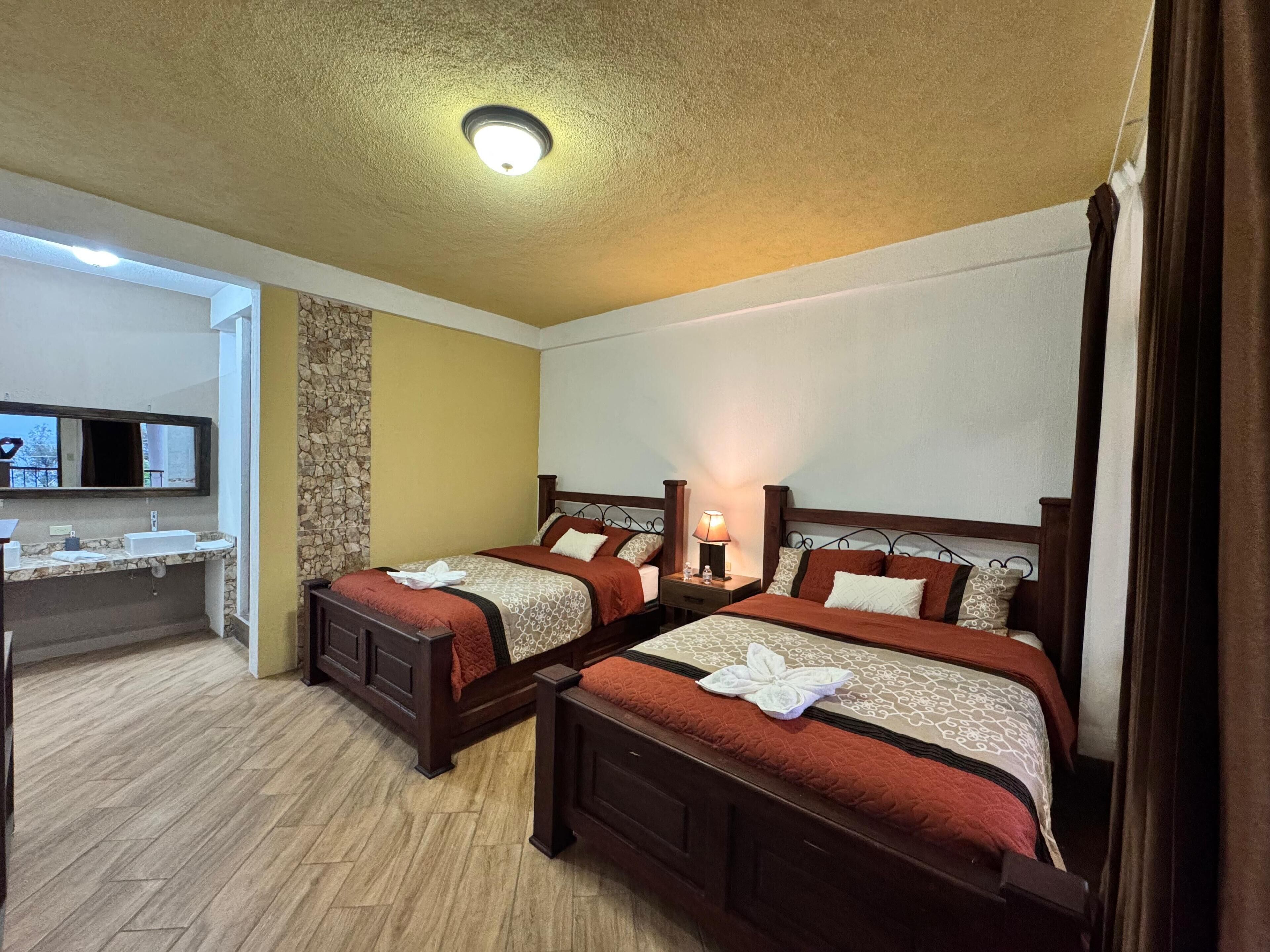 Camera d'albergo con due letti, bagno con parete in pietra decorativa e uno specchio grande.