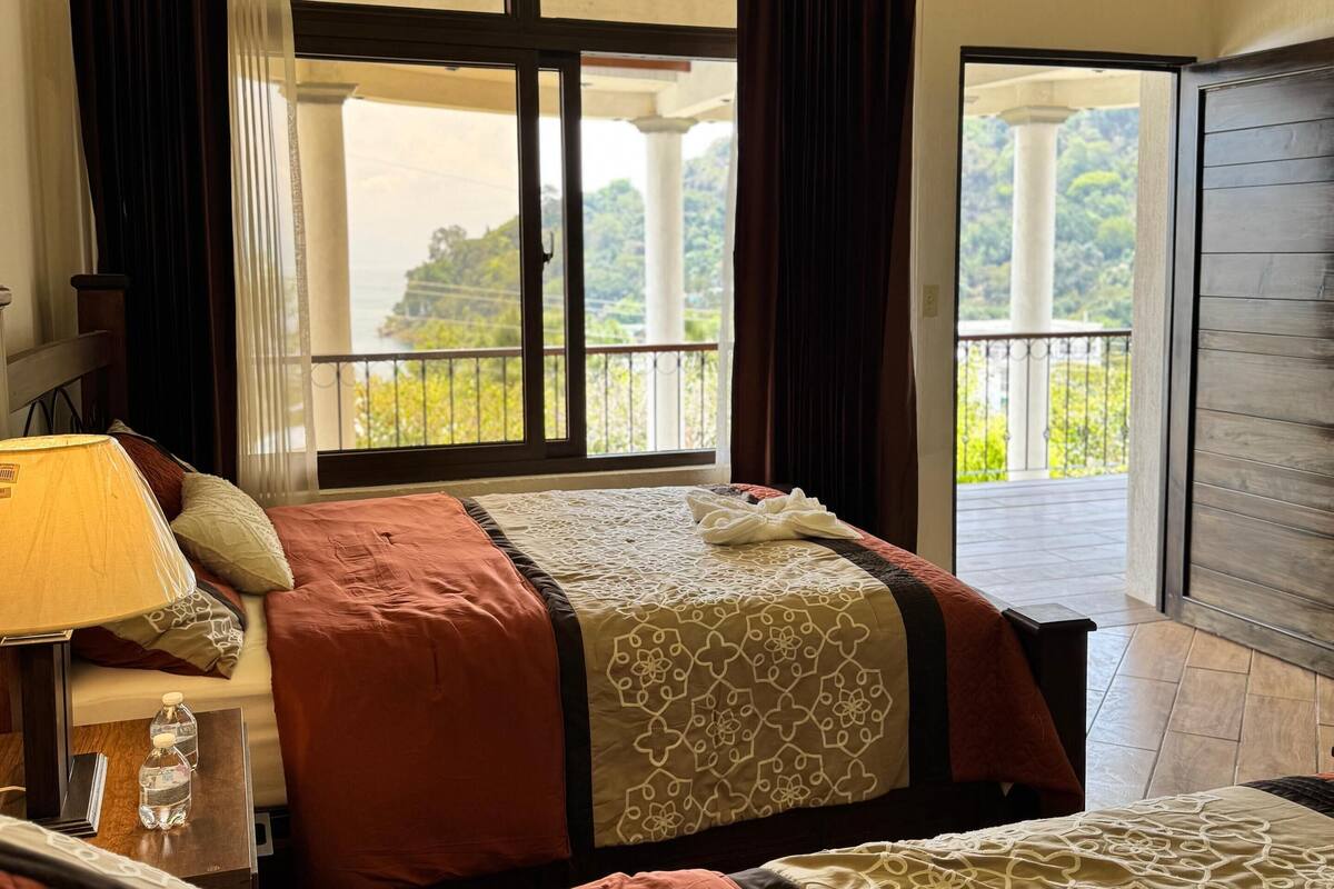 Een hotelkamer met twee bedden, een balkon en uitzicht op groen.