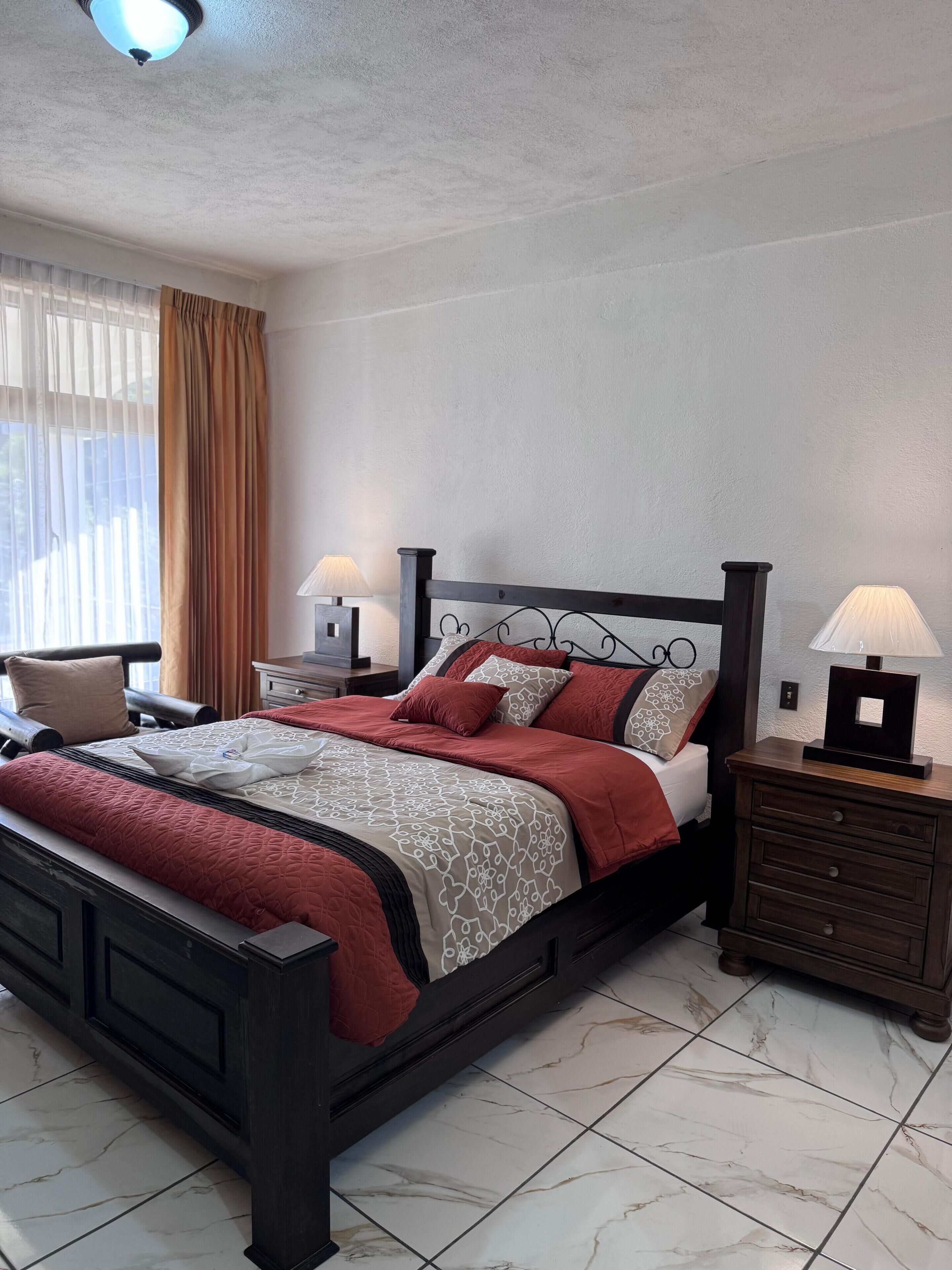 Une chambre à coucher bien rangée, avec un lit, des tables de chevet et une fenêtre avec des rideaux.