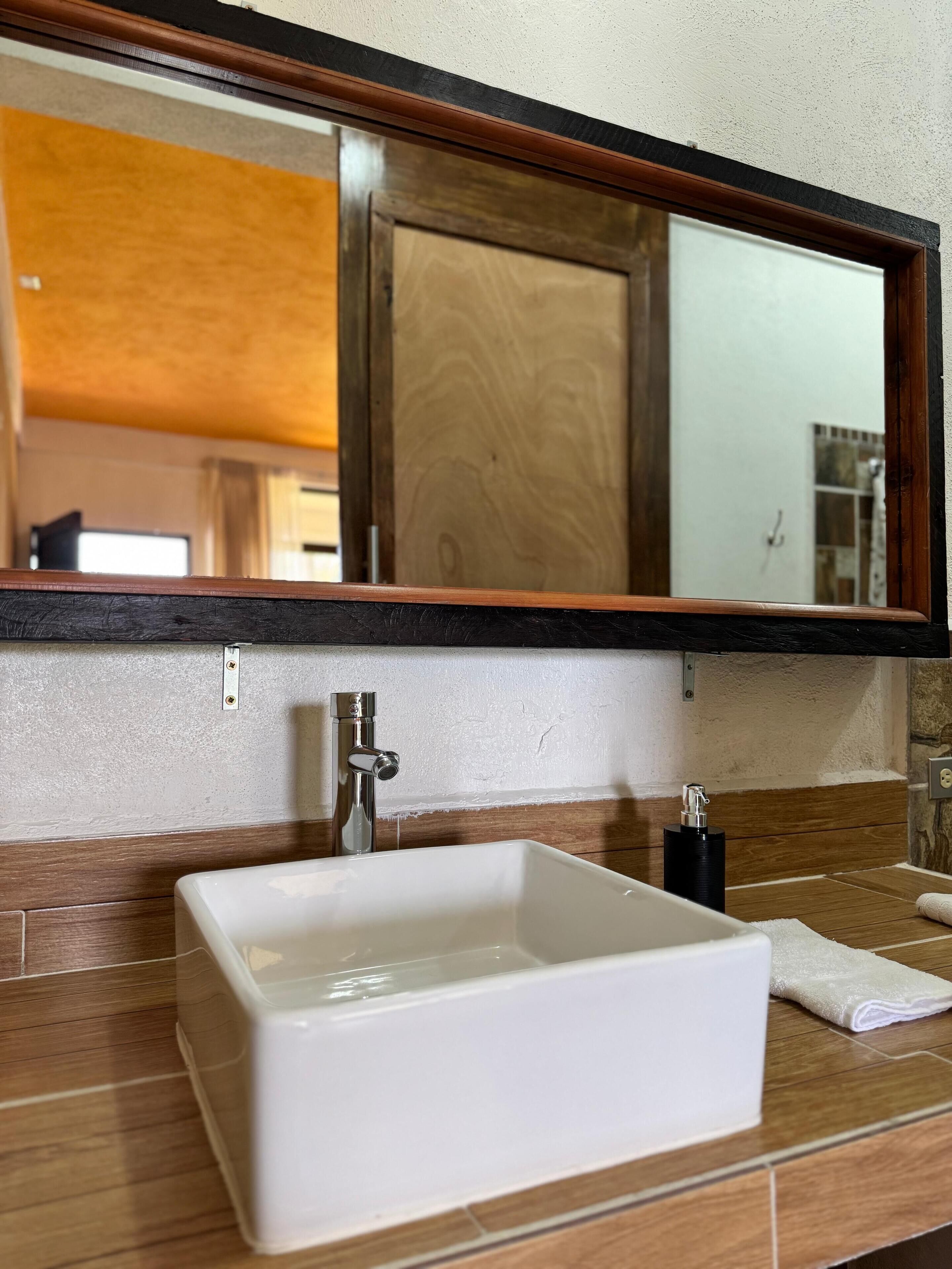 Een badkamer met een witte wastafel, een spiegel erboven en een houten opbergmeubel.