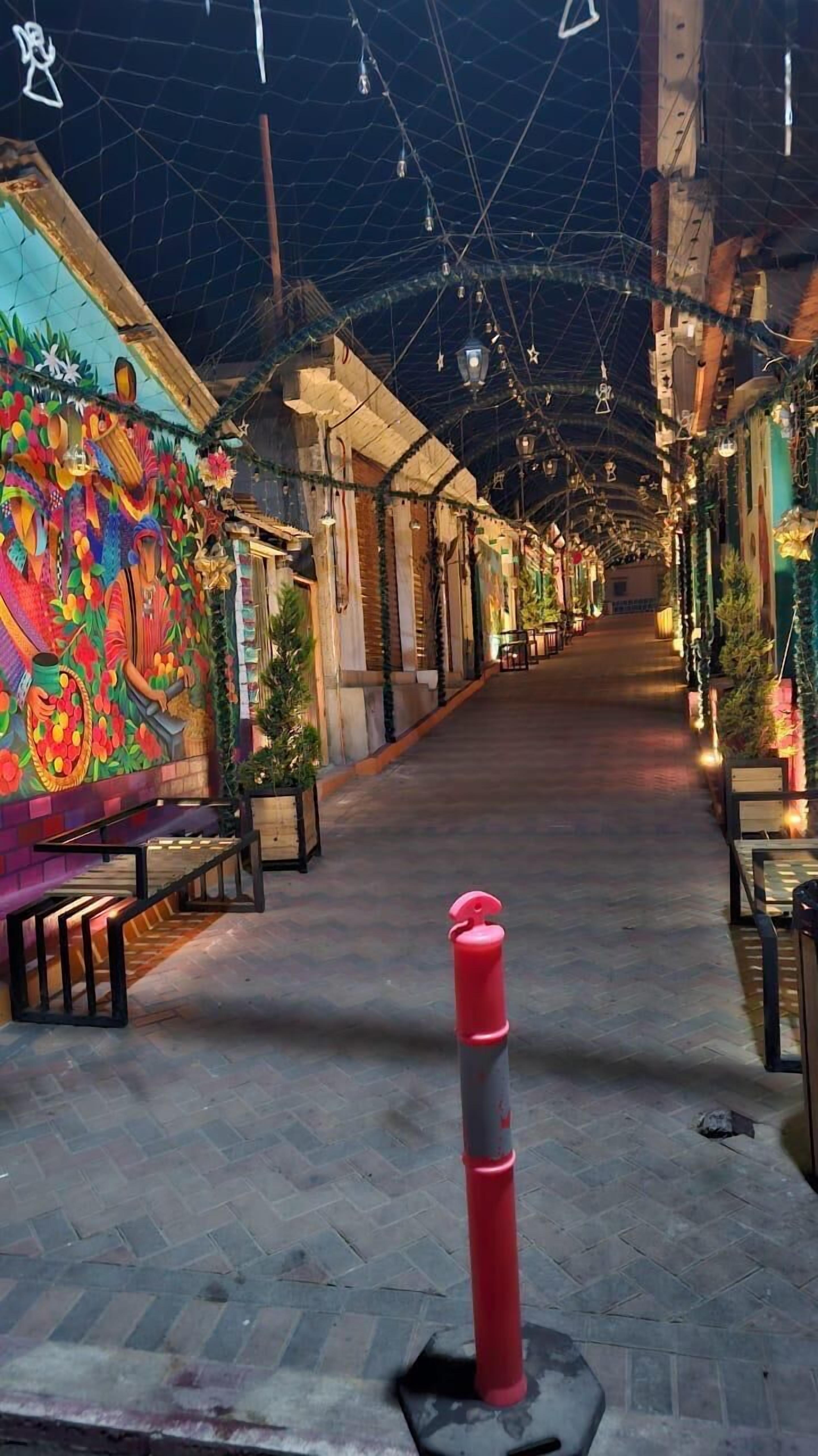 An indoor corridor with a tiled floor, benches, and a colorful mural on the left wall.