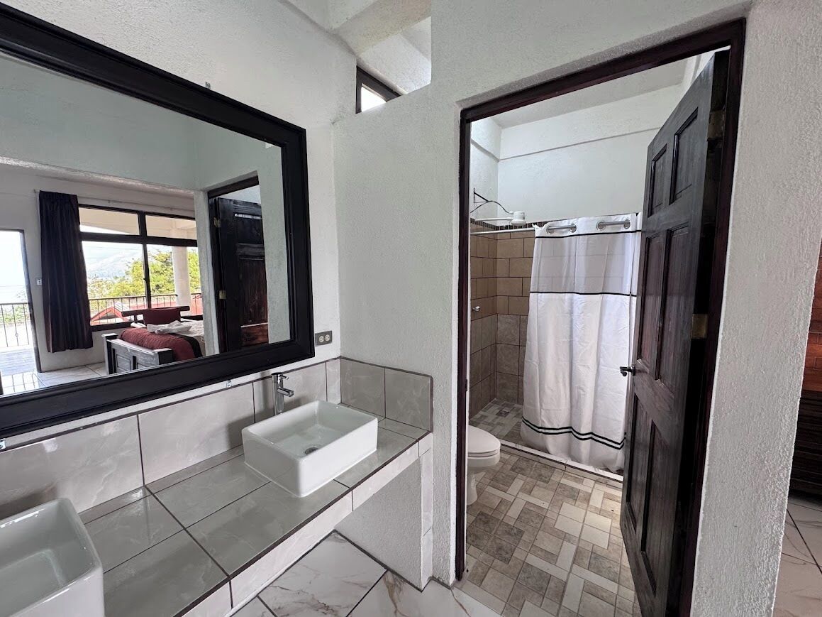 A bathroom with a large mirror, a glass sink, and a shower area.