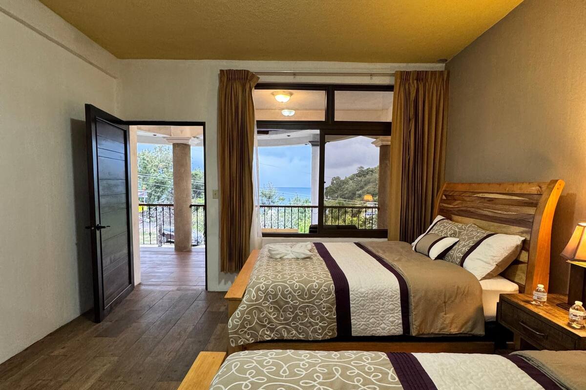 Een hotelkamer met twee bedden, een houten vloer, uitzicht op zee en een balkon.
