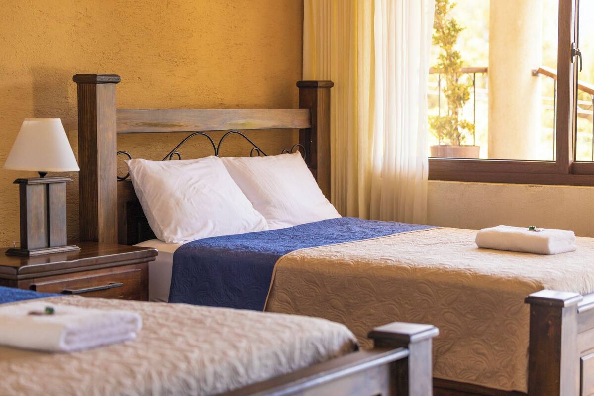 Een hotelkamer met twee bedden, een nachtkastje met een lamp en een raam met gordijnen.