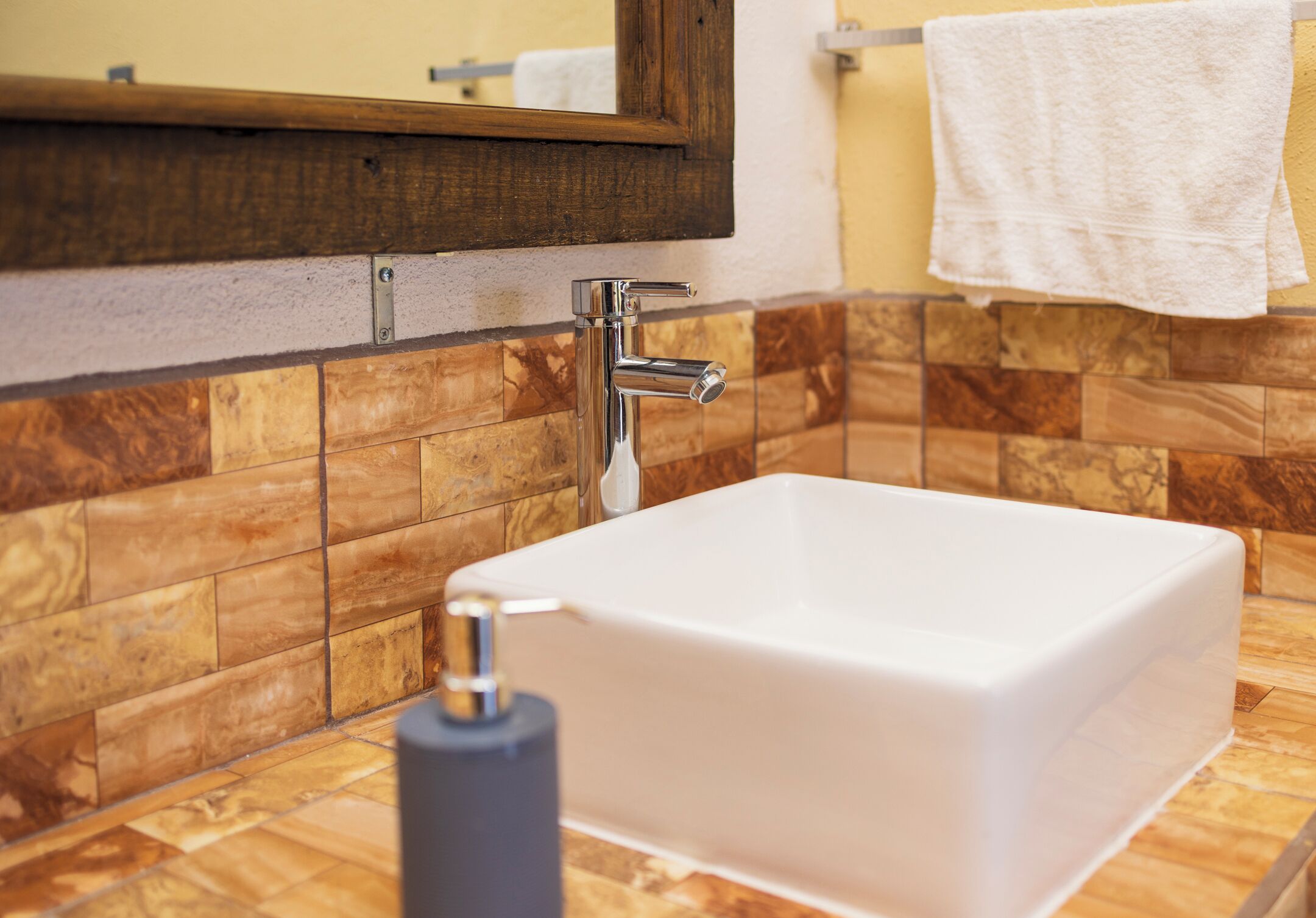 Un baño con un lavabo blanco, un tocador de madera, un espejo y una toalla colgada en la pared.